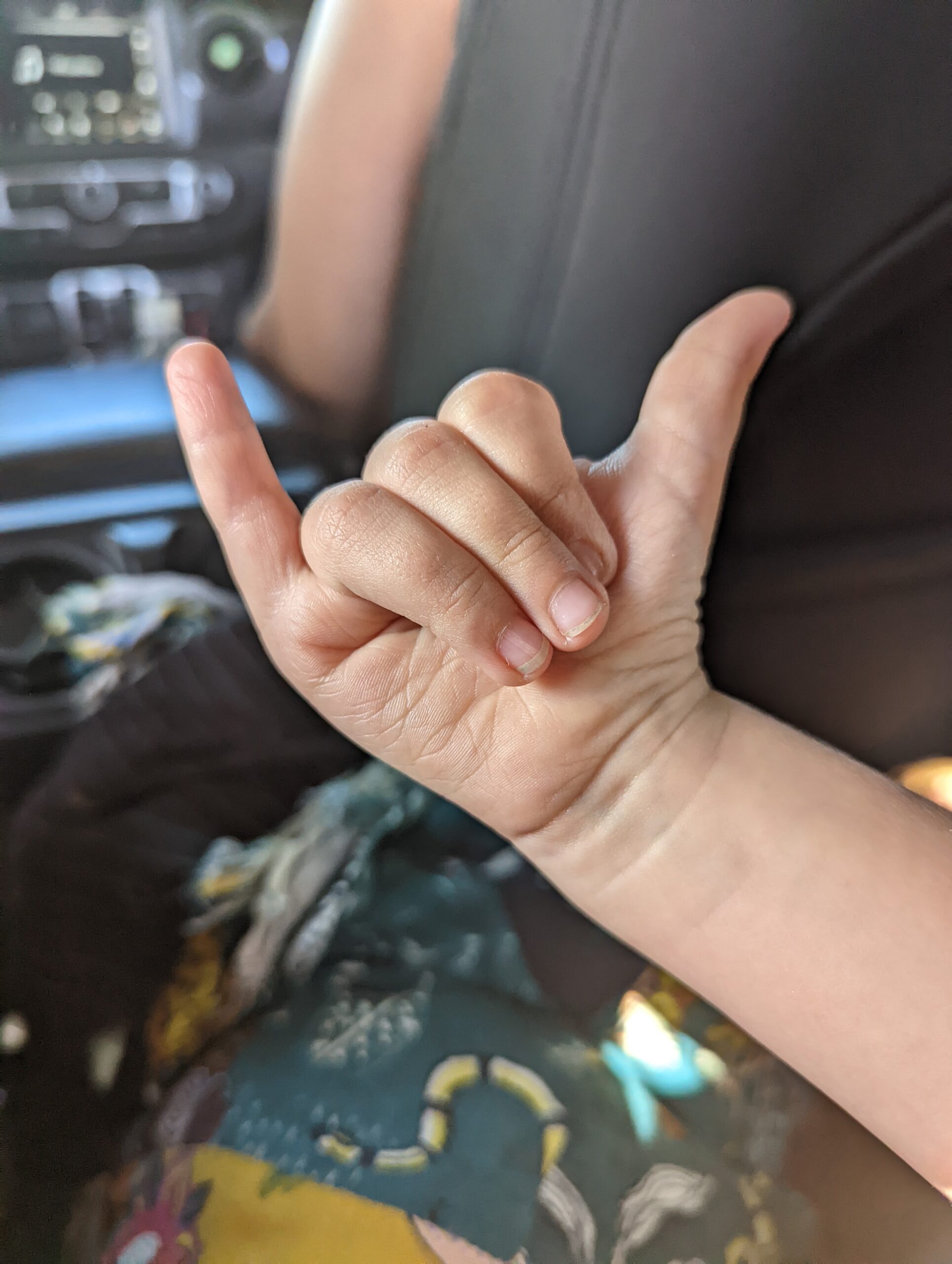 Close-up of a child’s hand making a shaka sign inside a car, symbolizing aloha spirit and friendly vibes in Hauʻula, Hawaiʻi