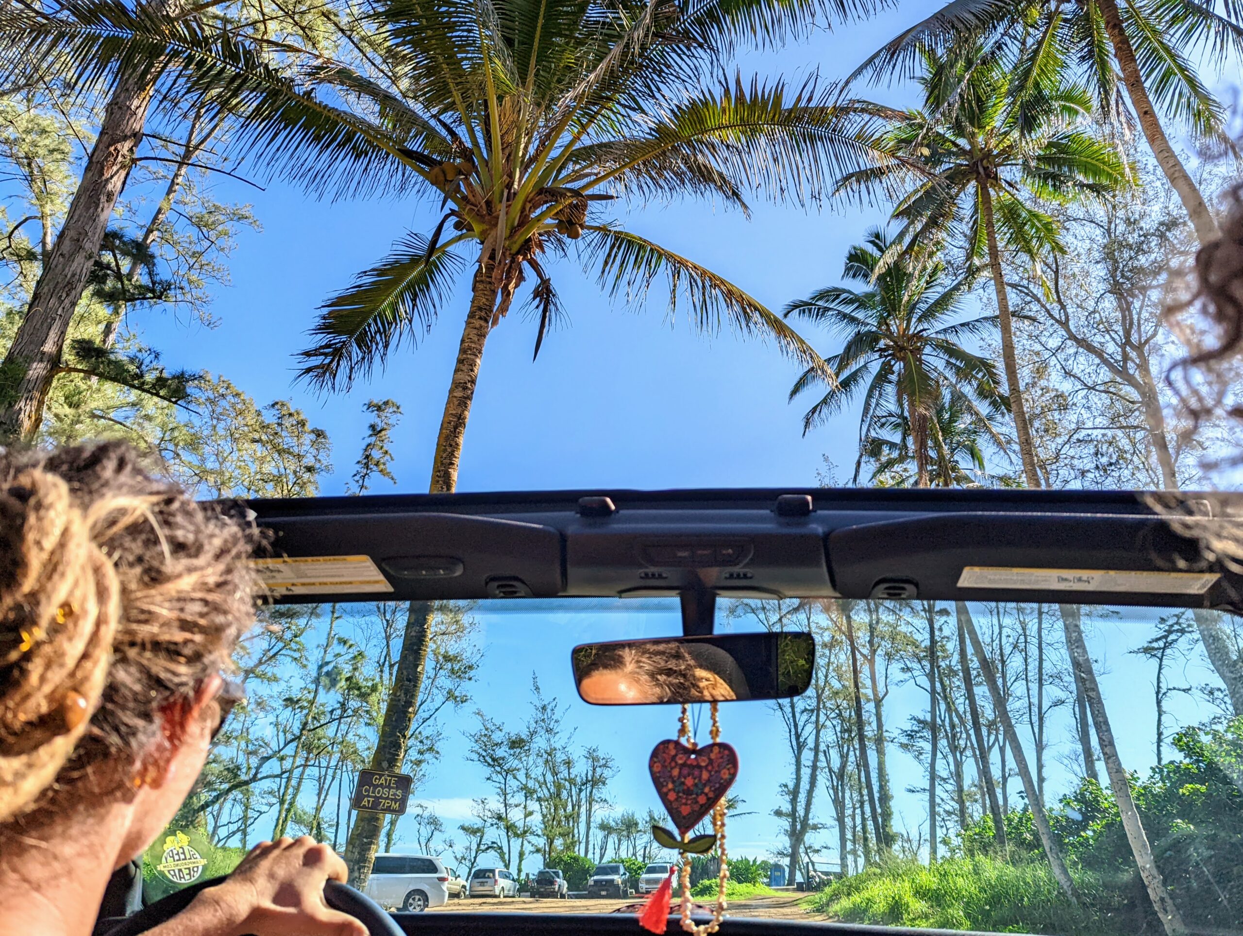 View from inside a Jeep driving under tall palm trees near the beach on Oʻahu’s North Shore, with blue skies and tropical scenery